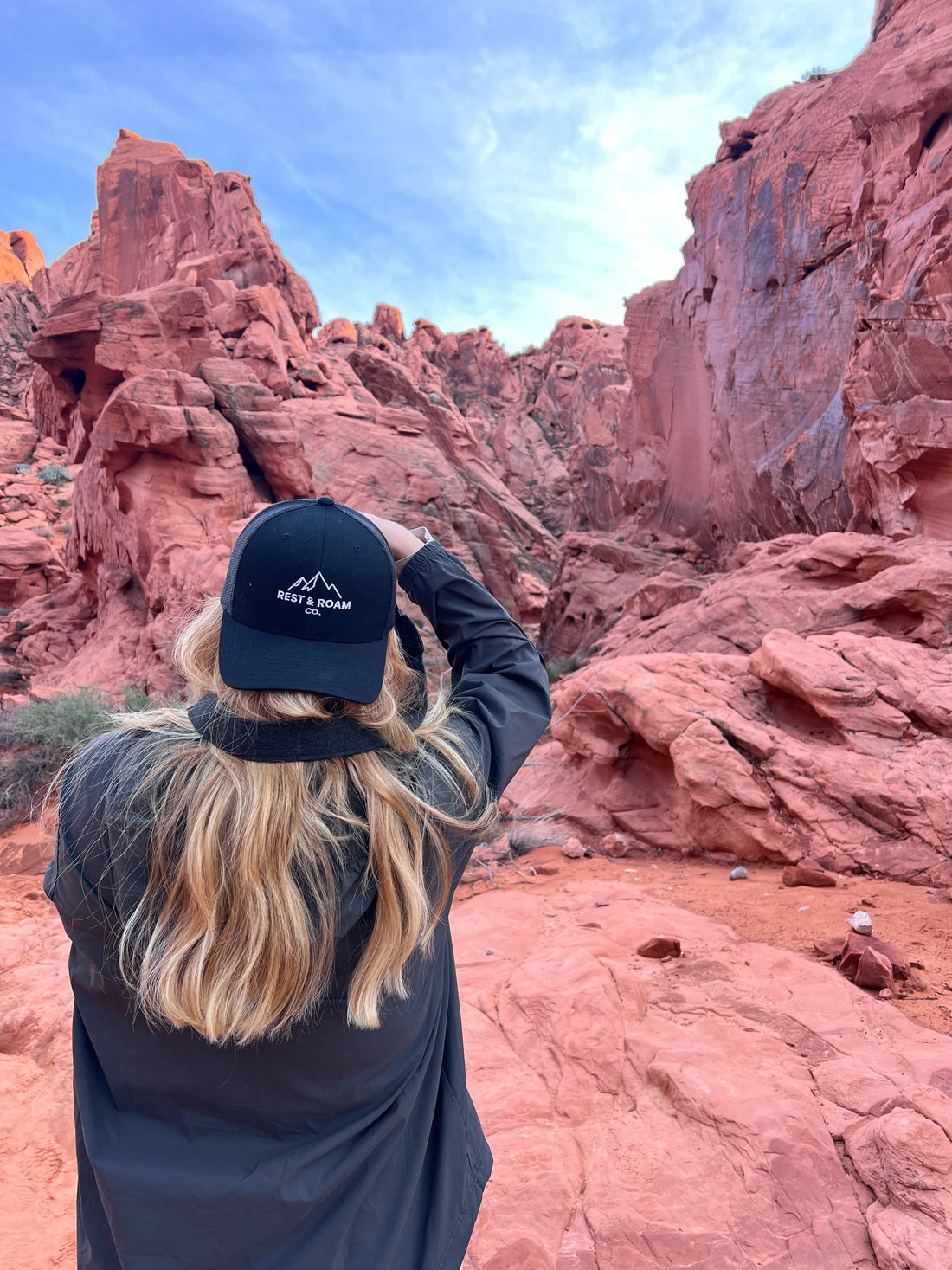 Woman wearing a black Rest & Roam Co. Trucker hat taking pictures of red rocks in Valley of Fire State Park 