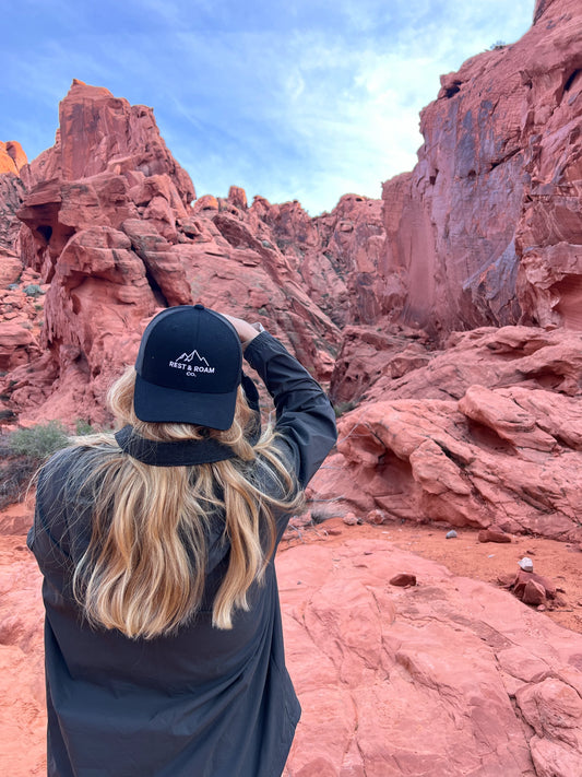 Woman wearing a black Rest & Roam Co. Trucker hat taking pictures of red rocks in Valley of Fire State Park 
