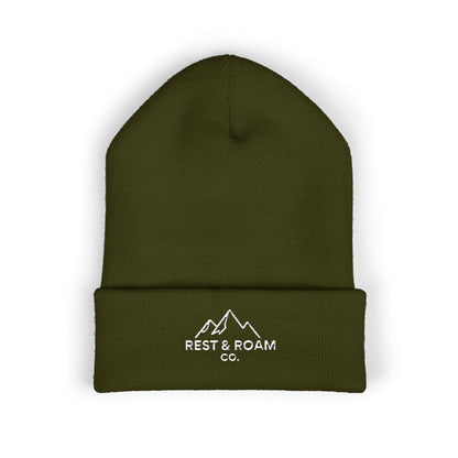 Flat lay of a cuffed knit olive beanie with small embroidered Rest & Roam Co. mountain logo on cuff.