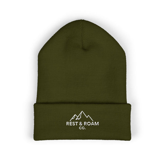Flat lay of a cuffed knit olive beanie with small embroidered Rest & Roam Co. mountain logo on cuff.
