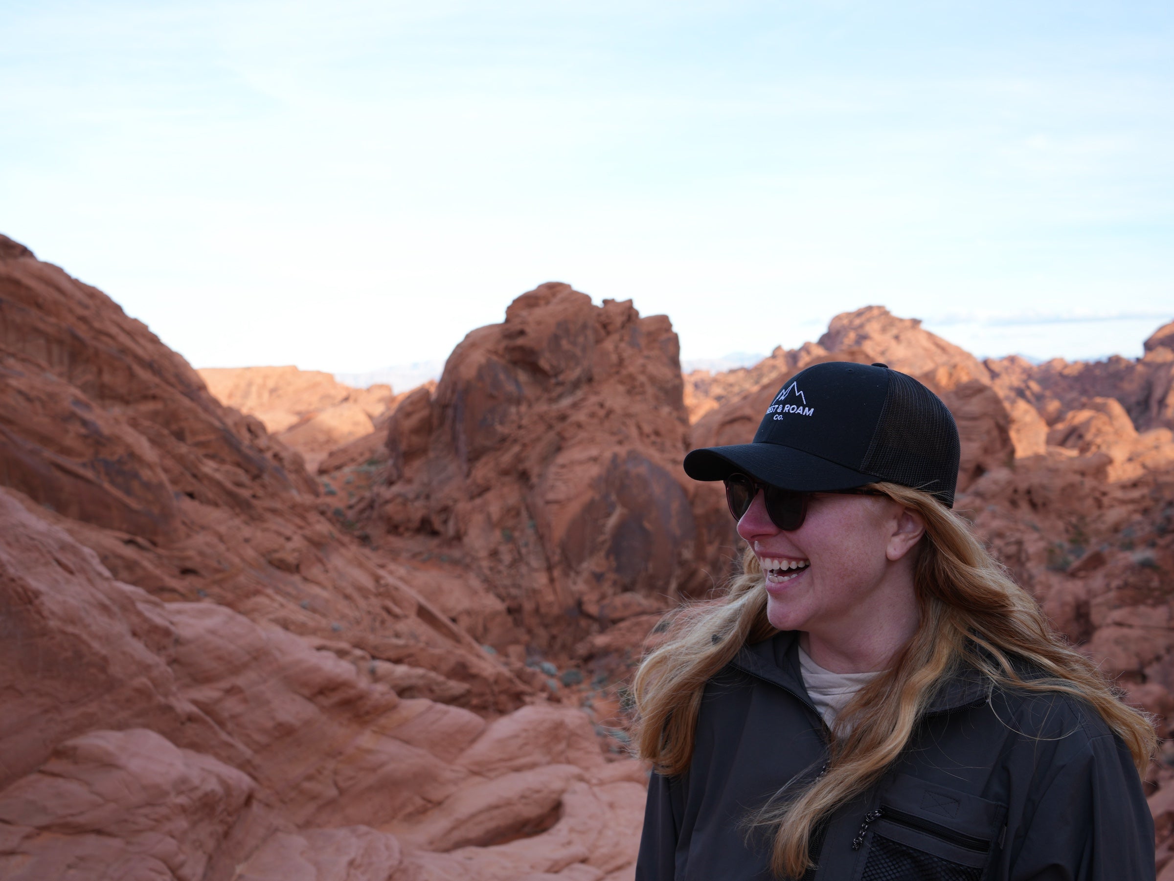 Woman wearing Rest & Roam Co. Trucker hat at Valley of Fire standing near red rocks