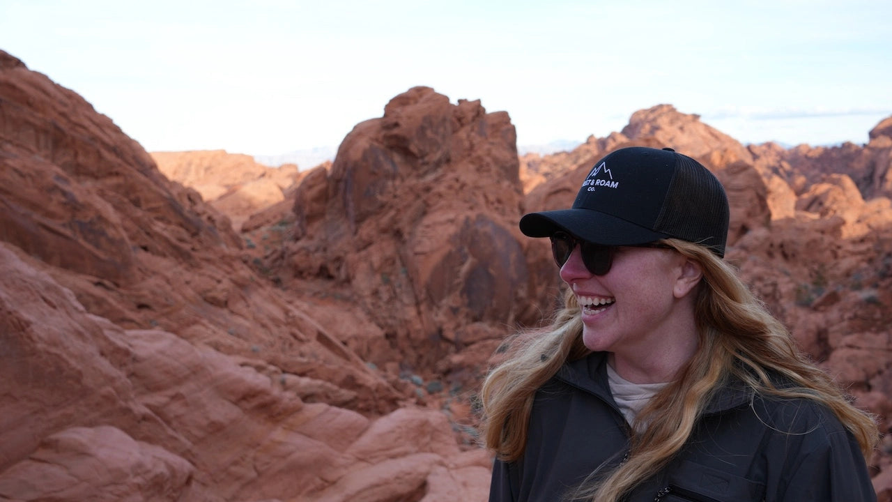 Woman wearing a black Rest & Roam Co. embroidered trucker hat with red rocks in the background